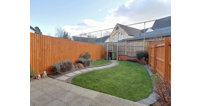 French doors from the kitchen lead out onto a tidy, landscaped rear garden with paved patio area and a well-kept lawn.