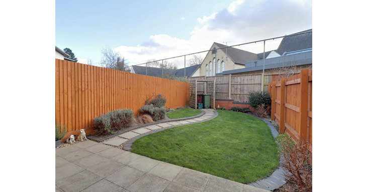 French doors from the kitchen lead out onto a tidy, landscaped rear garden with paved patio area and a well-kept lawn.