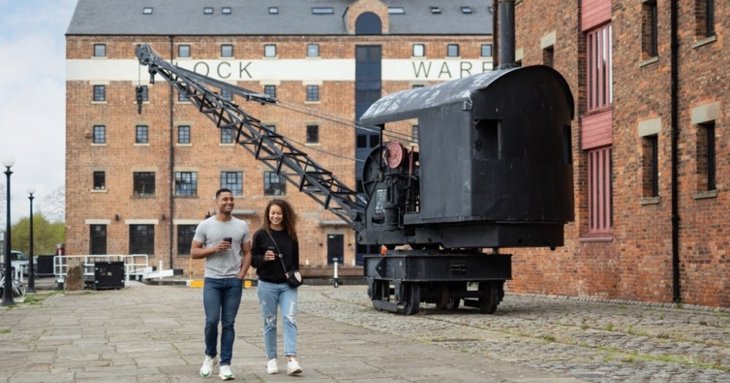 A young couple with takeaway coffees walk around Gloucester Docks in Gloucestershire, UK.